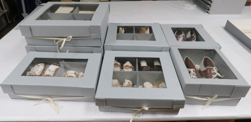 Seven blueboard boxes of varying sizes, holding between one and four pairs of children's shoes.