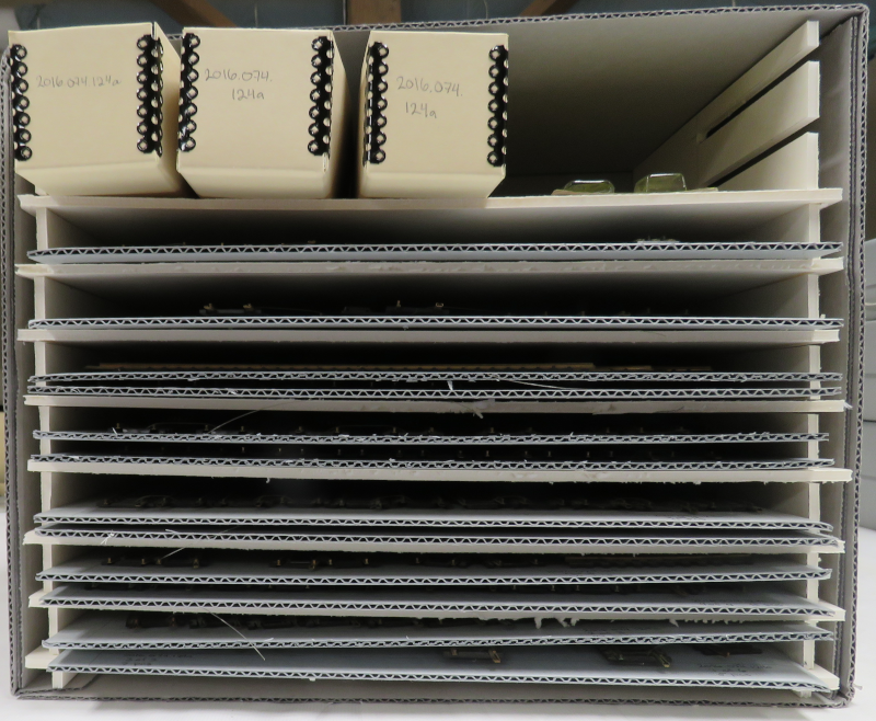 A shelf structure made of cream foamcore inside a blueboard crate, with pieces of blueboard visible on 7 of the 8 shelves.